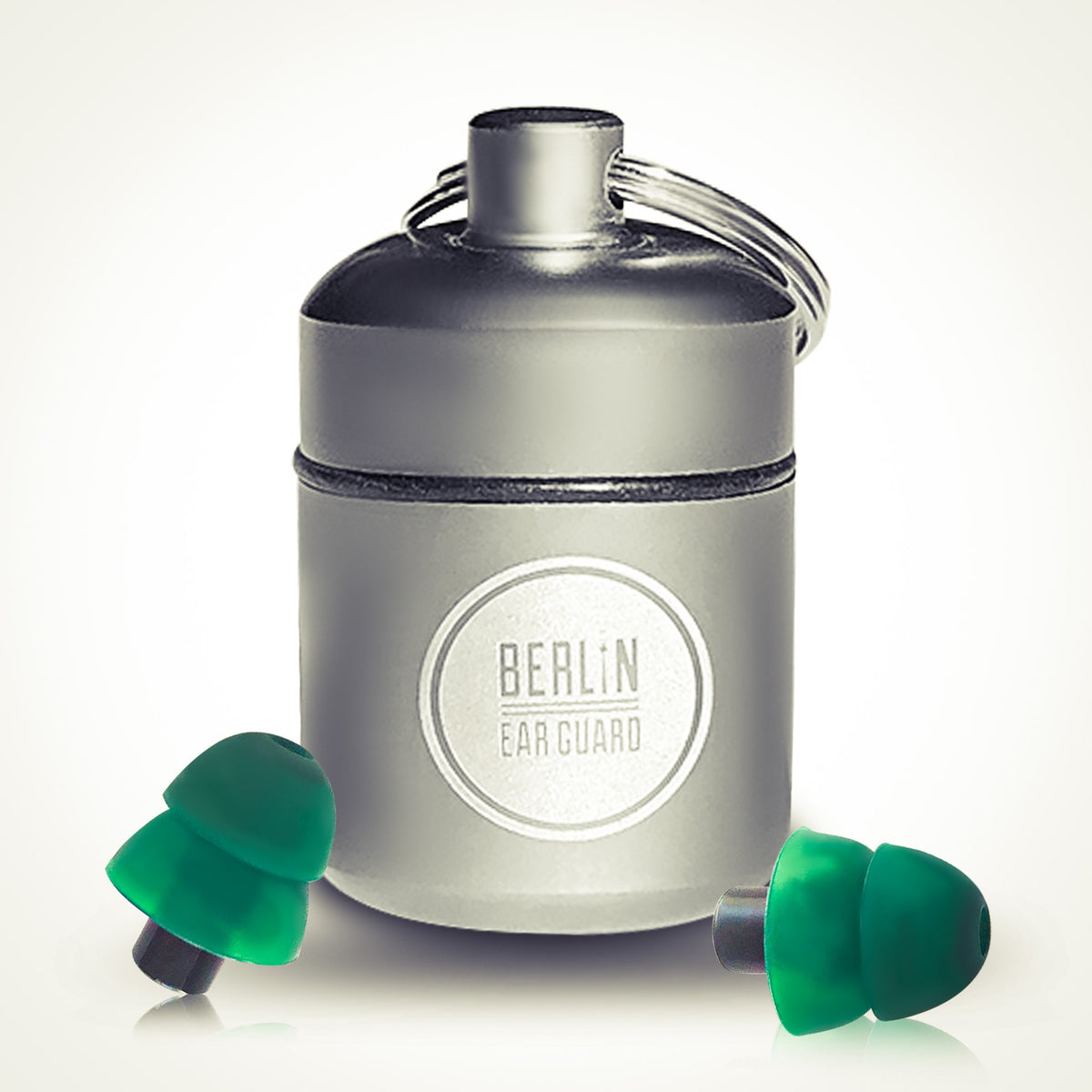 Ein Paar grüne Ohrstöpsel und ein kleines silbernes Etui mit der Aufschrift "Berlin Ear Guard" und einem Schlüsselanhänger, dargestellt vor einem schlichten Hintergrund.