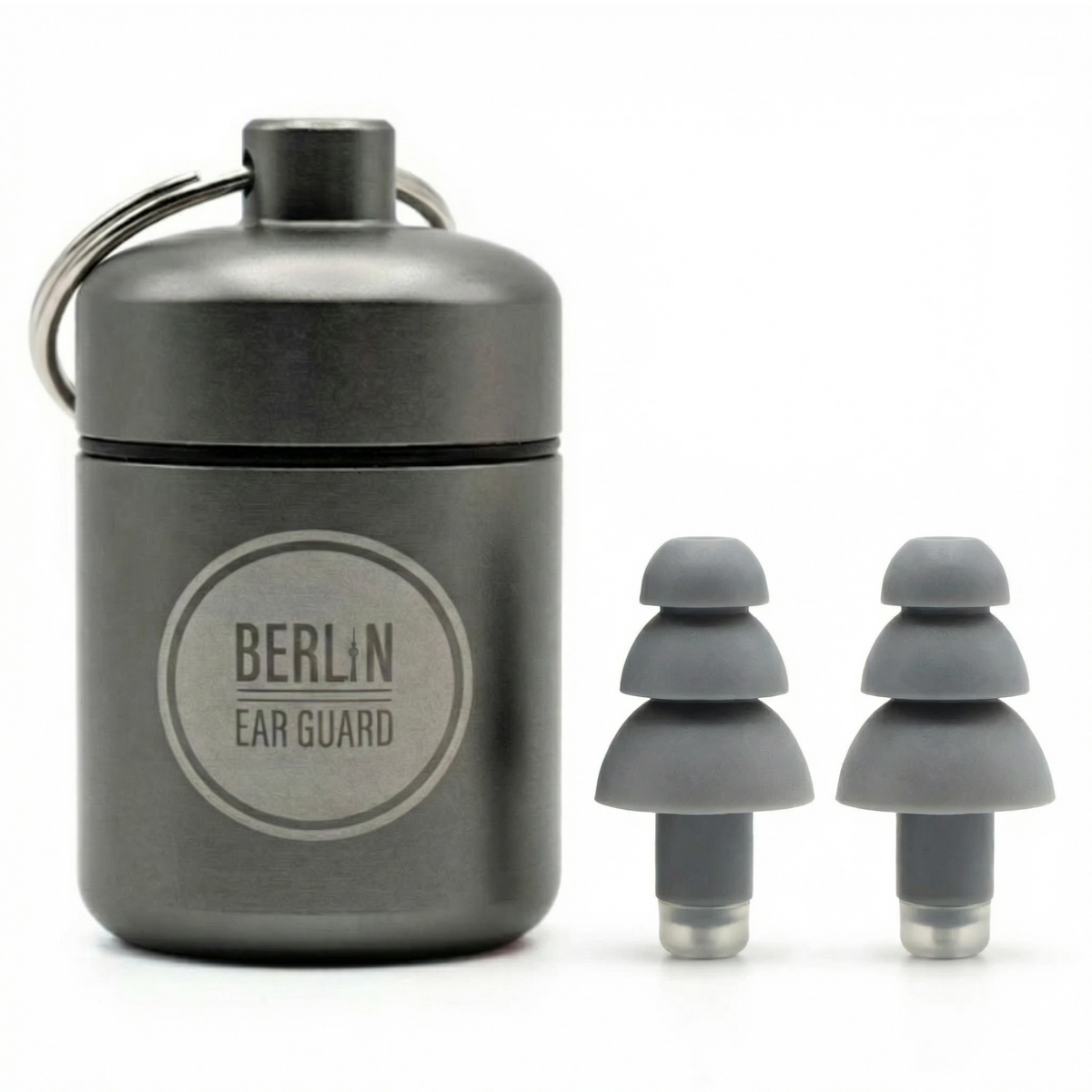 Ohrstöpsel "Lehrer in Neukölln"stehen auf dem Tisch. Daneben steht der hochwertige Aufbewahrungsbehälter im Schlüsselanhänger Format mit der Aufschrift "Berlin Ear Guard"